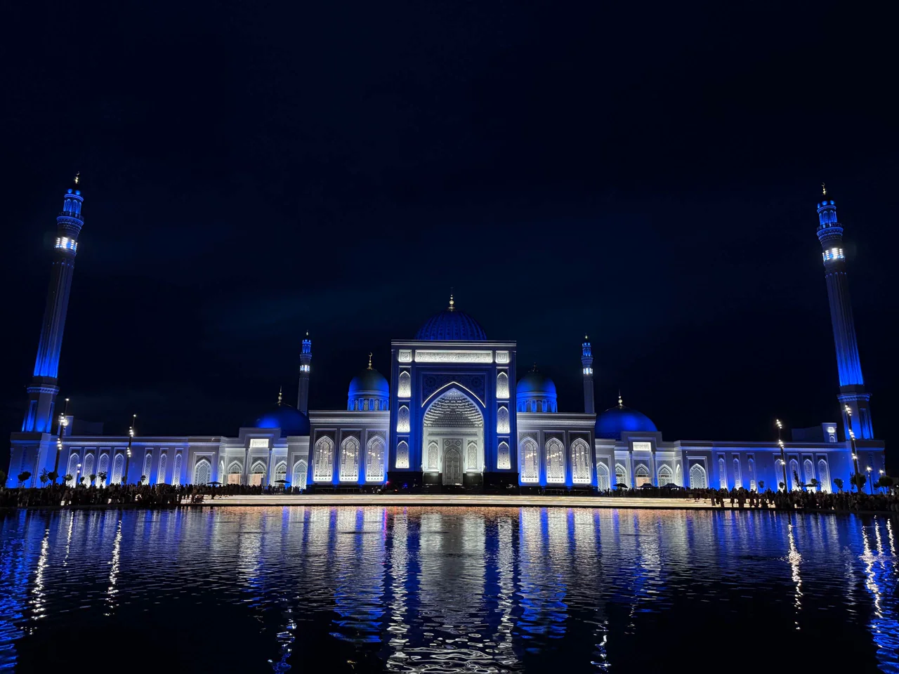 A mosque floodlit blue at night, mirrored in the pool in front of it